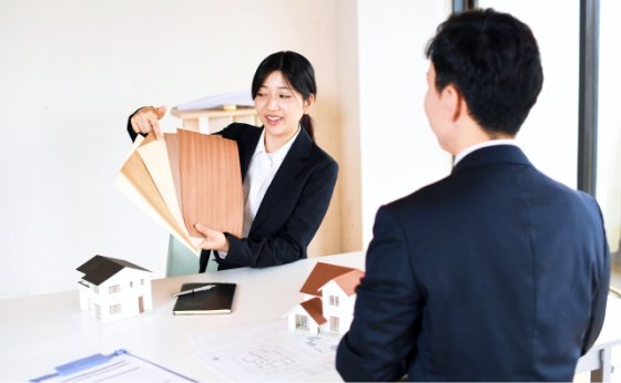 スーツを着た女性スタッフが男性に向かって商材を手に持ち説明をしている