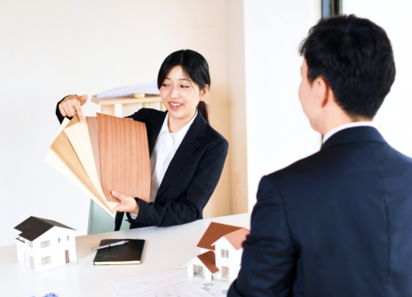 スーツを着た女性スタッフが男性に向かって商材を手に持ち説明をしている